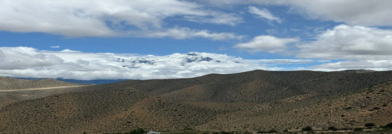 Snowy peaks and arid hills under a vibrant blue sky